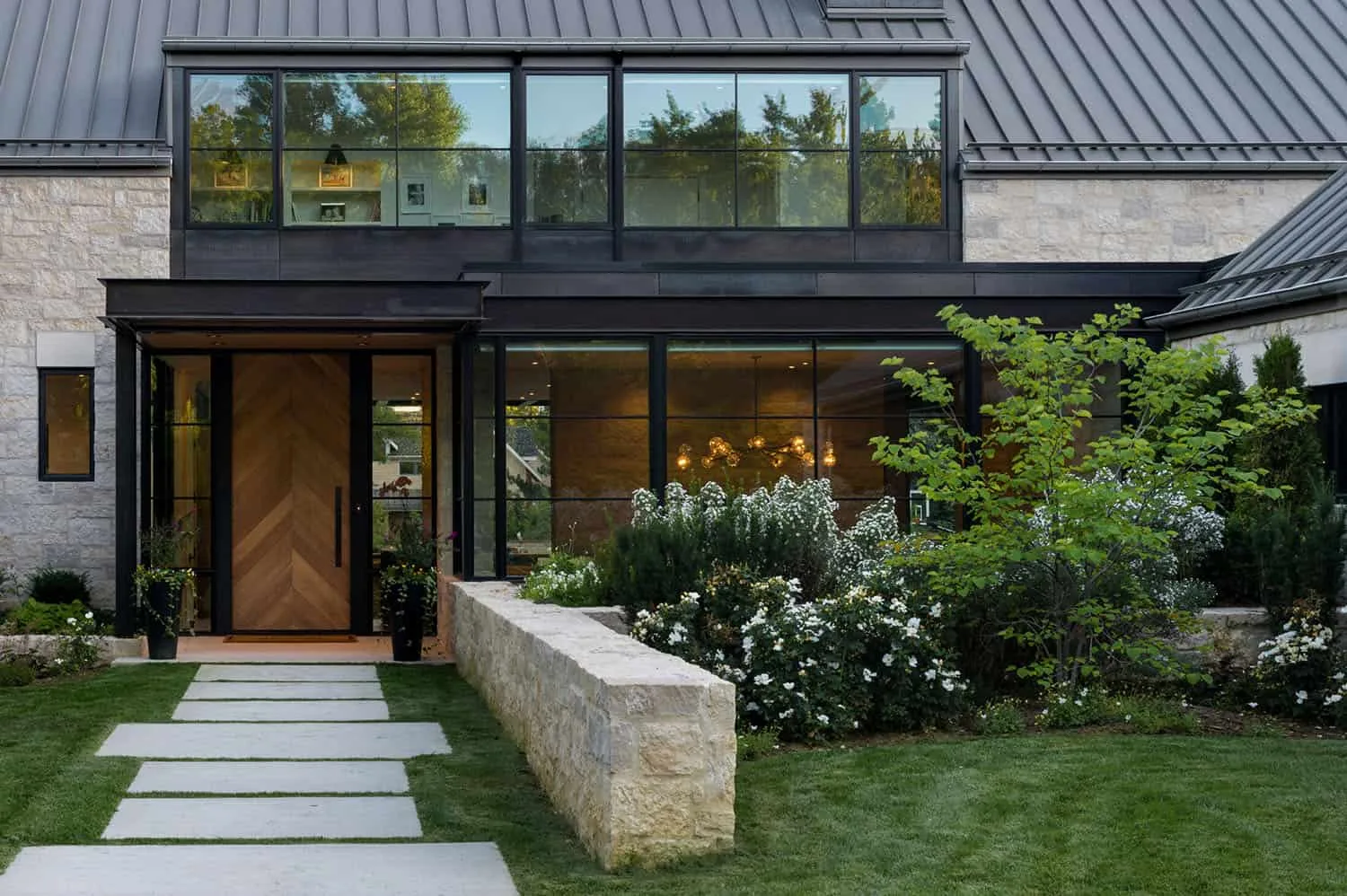Modern stone and glass home with a chevron wood front door, seen from the front walk