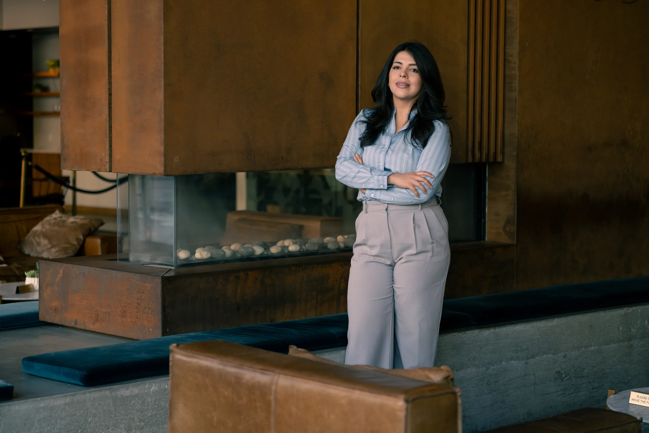 Ruby Medina standing with arms crossed in a warm, modern lounge